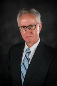 A man in a suit and tie standing up against a black background.