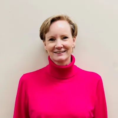 A woman in a pink shirt standing next to a wall.