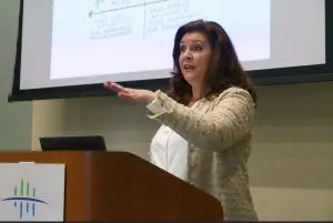 A woman standing at a podium in front of a projector screen.