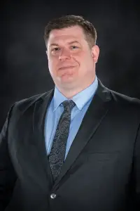 A man in a suit and tie standing up against a black background.